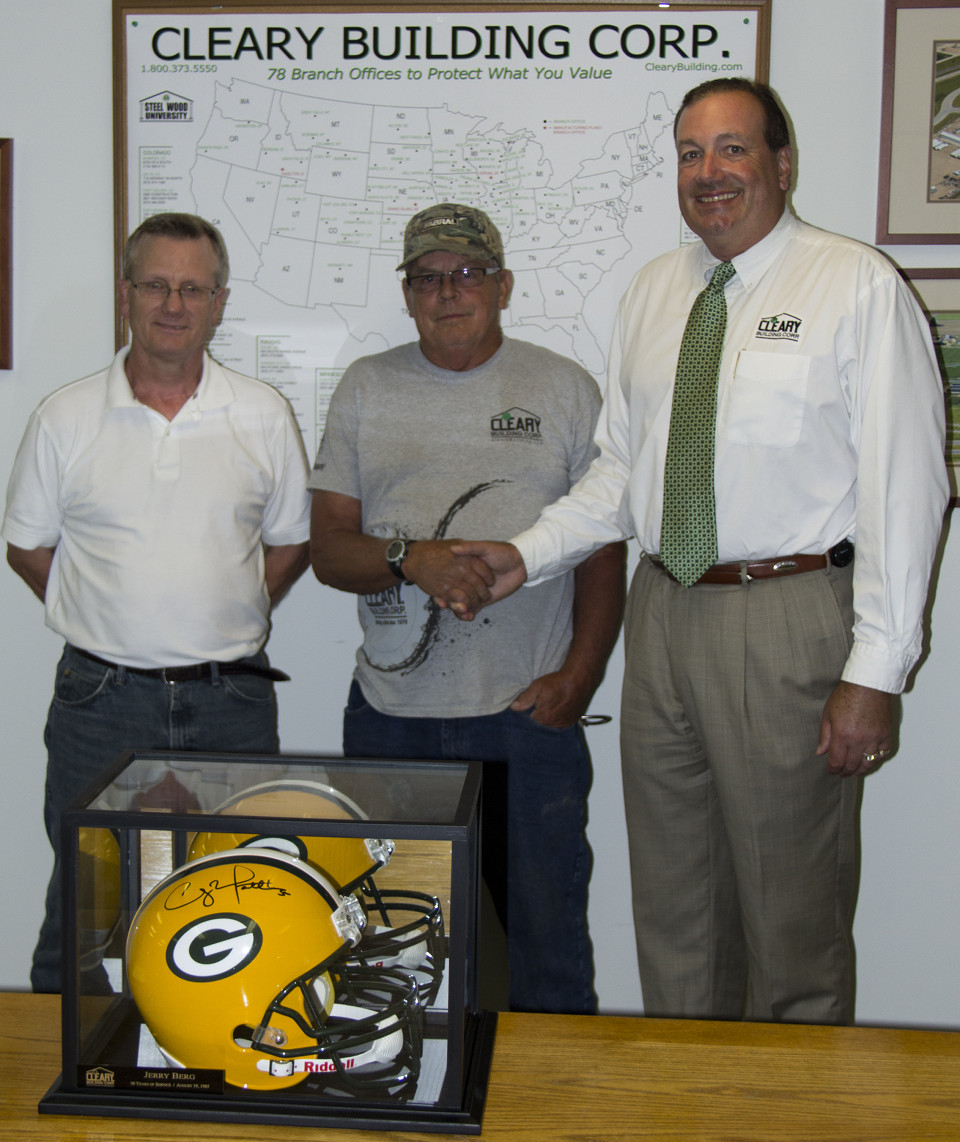 Jerry shakes hands with Sean Cleary while Dan stands to the side. Packers helmet sits on the table in front of them.