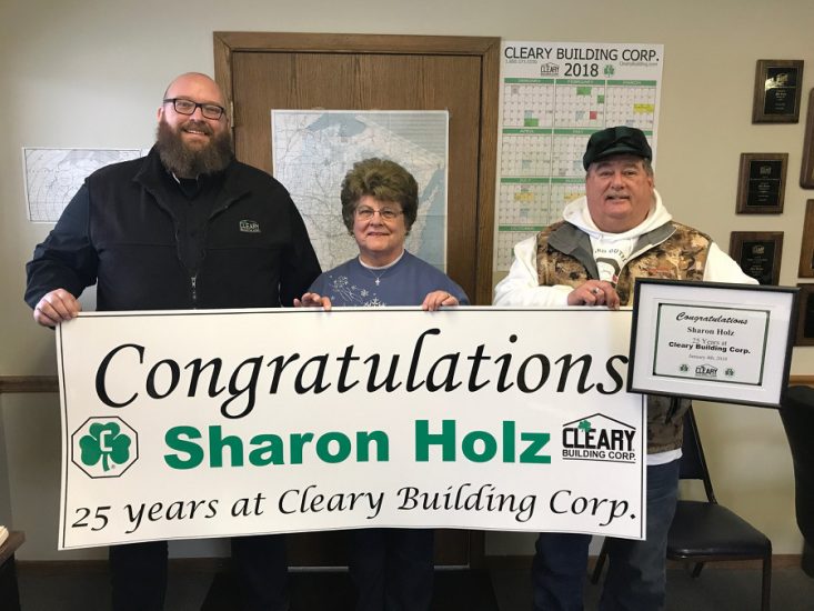 Sharon and two men hold congratulatory banner.