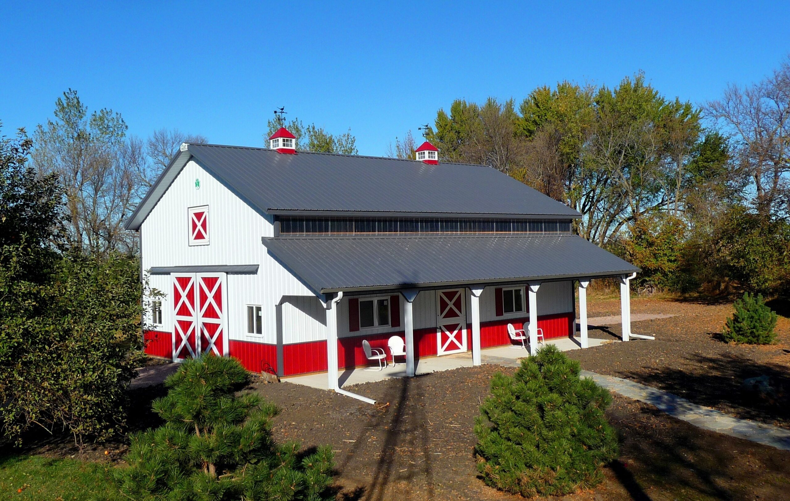 White and red barn with a large porch and cupolas.
